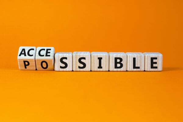 Wooden cubes on an orange background, with the first two cubes partially rotated to reveal the word 'accessible' from 'possible.